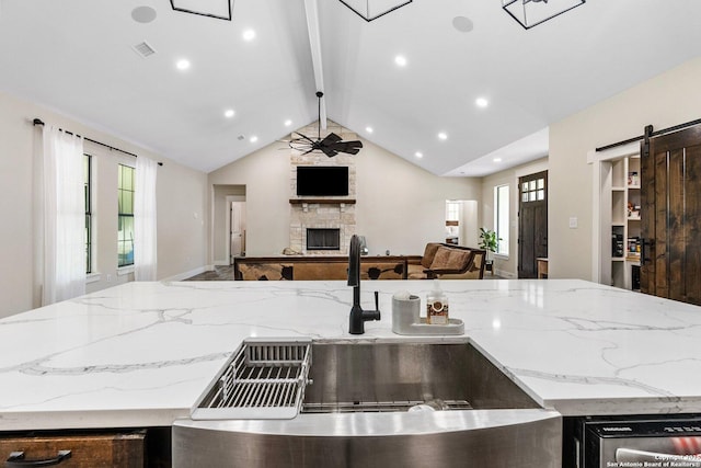 kitchen featuring vaulted ceiling with beams, a stone fireplace, light stone countertops, and a barn door