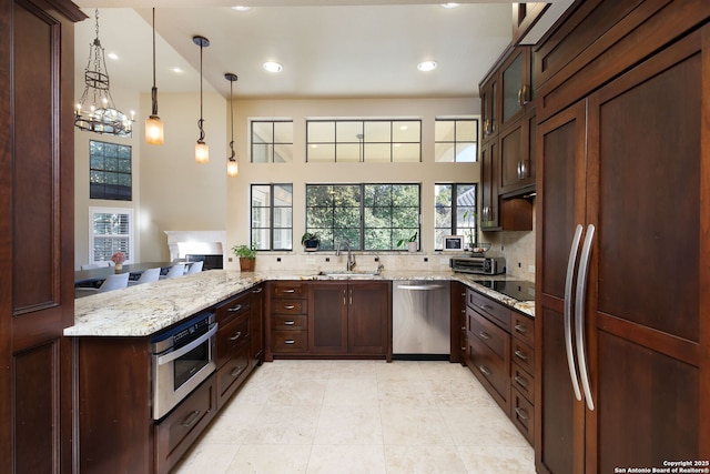 kitchen featuring pendant lighting, sink, stainless steel appliances, light stone counters, and kitchen peninsula