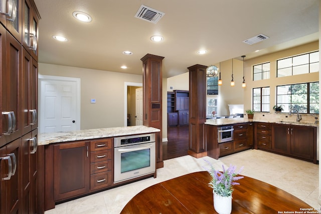 kitchen with sink, decorative columns, decorative light fixtures, kitchen peninsula, and stainless steel oven