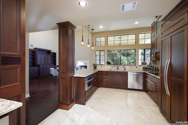 kitchen featuring sink, appliances with stainless steel finishes, kitchen peninsula, pendant lighting, and light stone countertops