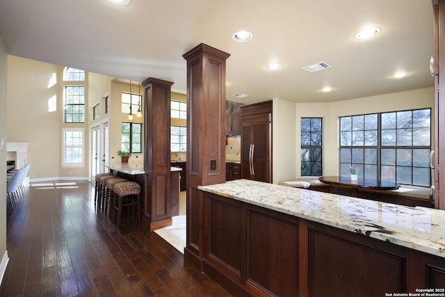 kitchen featuring hanging light fixtures, decorative columns, light stone countertops, paneled fridge, and dark hardwood / wood-style flooring