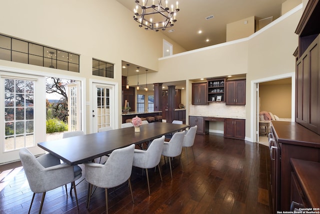 dining area with an inviting chandelier, built in desk, dark hardwood / wood-style floors, and a high ceiling