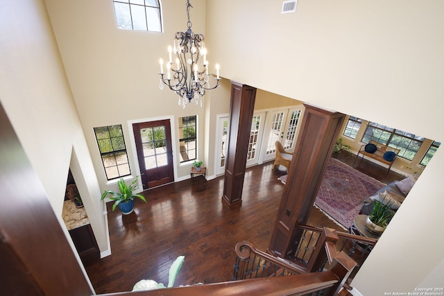 foyer with a towering ceiling, dark hardwood / wood-style flooring, a chandelier, and ornate columns