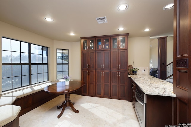 kitchen with light stone counters, kitchen peninsula, decorative columns, and light tile patterned floors