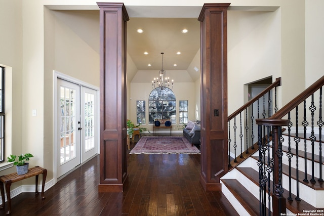 foyer entrance with french doors, an inviting chandelier, dark hardwood / wood-style flooring, a towering ceiling, and decorative columns