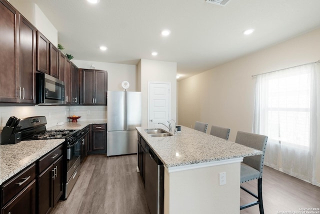 kitchen featuring sink, tasteful backsplash, light wood-type flooring, appliances with stainless steel finishes, and a kitchen breakfast bar