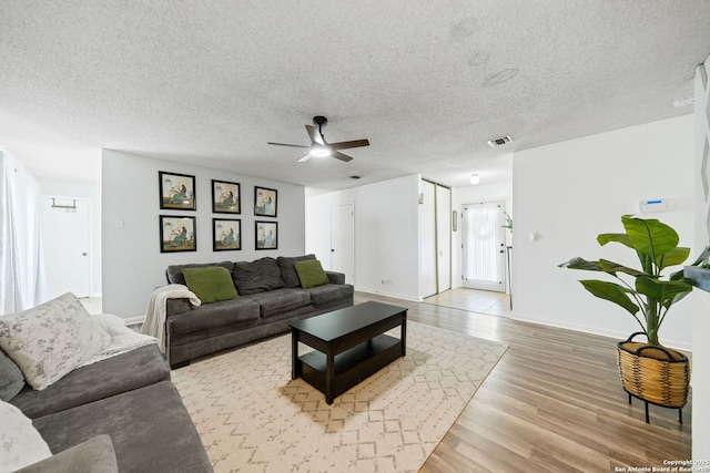 living room featuring ceiling fan, light hardwood / wood-style flooring, and a textured ceiling