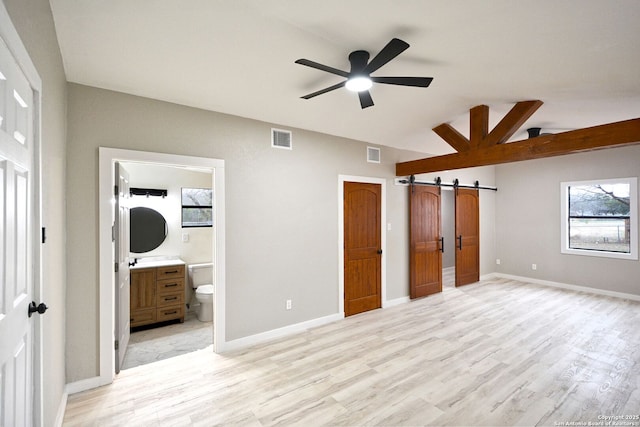 unfurnished bedroom featuring multiple windows, light hardwood / wood-style flooring, lofted ceiling, and a barn door