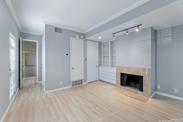 unfurnished living room with a high end fireplace, ornamental molding, rail lighting, and light wood-type flooring