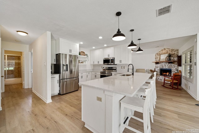 kitchen featuring pendant lighting, sink, stainless steel appliances, white cabinets, and a kitchen bar