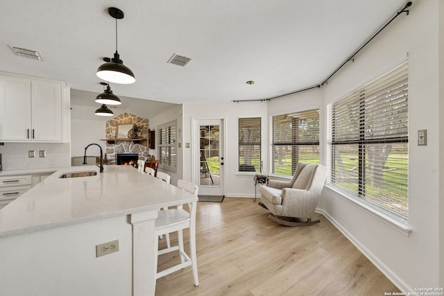 kitchen featuring sink, decorative light fixtures, a stone fireplace, and white cabinets