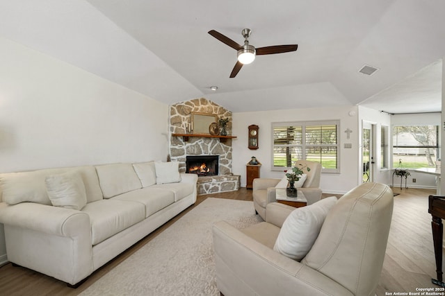 living room with vaulted ceiling, a stone fireplace, ceiling fan, and light wood-type flooring