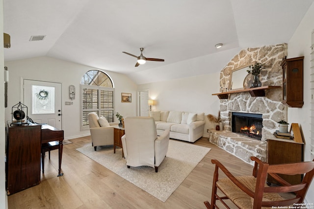 living room featuring ceiling fan, lofted ceiling, a stone fireplace, and light hardwood / wood-style floors