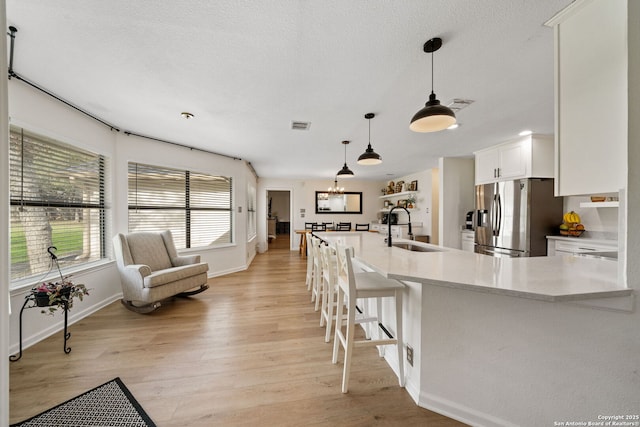 kitchen featuring pendant lighting, sink, white cabinetry, stainless steel refrigerator with ice dispenser, and light wood-type flooring