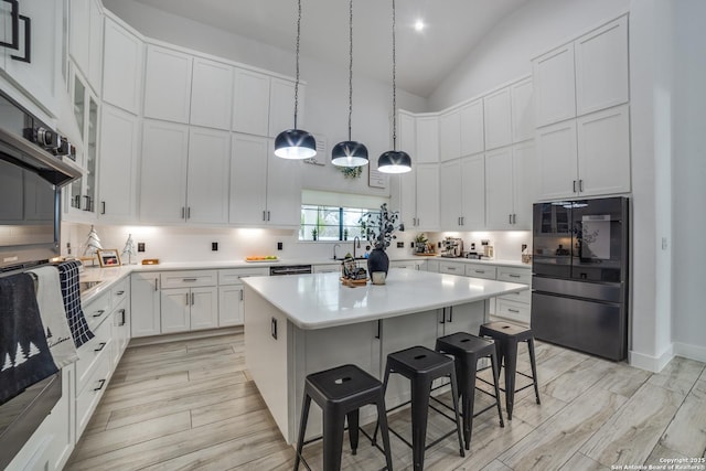 kitchen featuring a breakfast bar, white cabinetry, fridge, a kitchen island, and decorative light fixtures