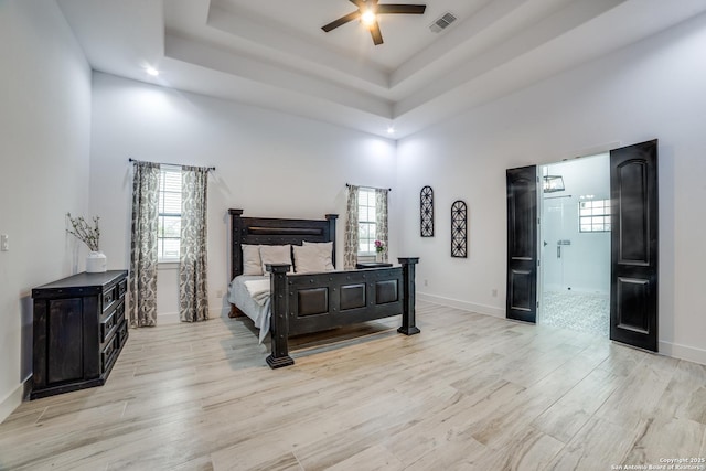 bedroom featuring a tray ceiling, light hardwood / wood-style floors, ceiling fan, and a high ceiling