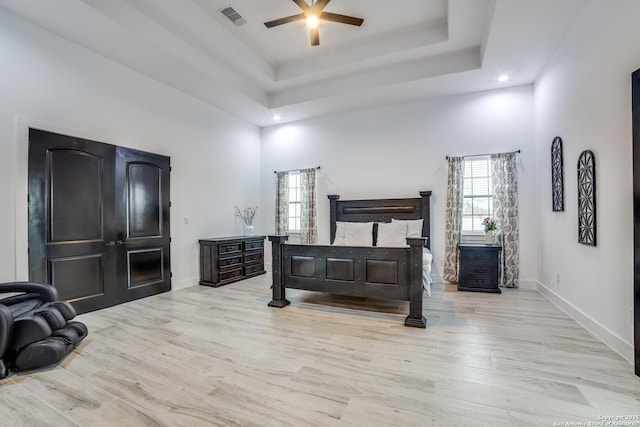 bedroom with ceiling fan, a raised ceiling, multiple windows, and light hardwood / wood-style flooring