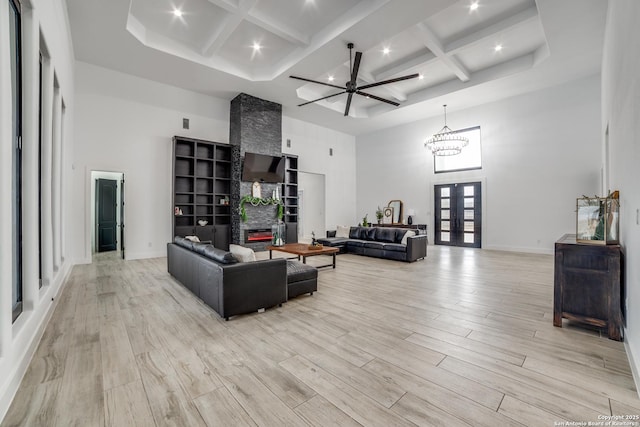 living room with french doors, coffered ceiling, light hardwood / wood-style flooring, ceiling fan with notable chandelier, and a high ceiling