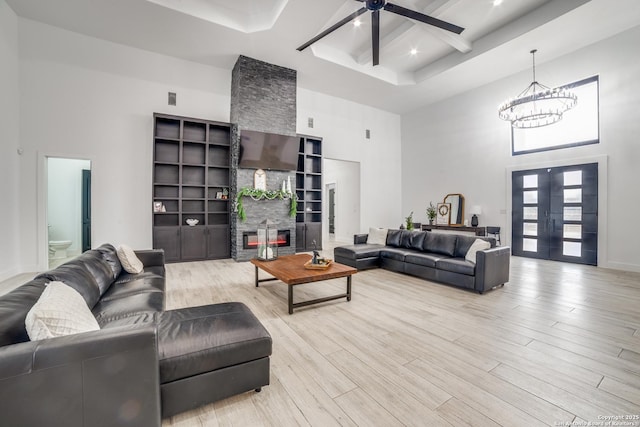 living room with built in shelves, french doors, a stone fireplace, light hardwood / wood-style flooring, and a towering ceiling