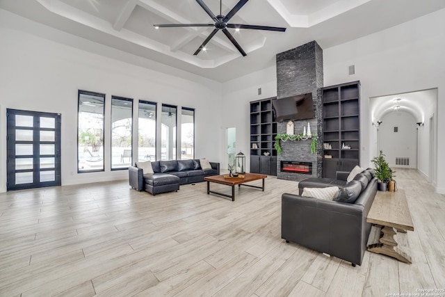 living room featuring coffered ceiling, beam ceiling, a stone fireplace, and a high ceiling