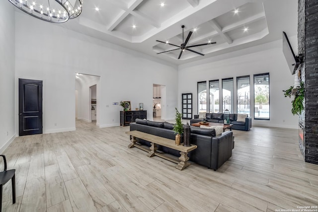 living room with a high ceiling, coffered ceiling, ceiling fan with notable chandelier, and beam ceiling