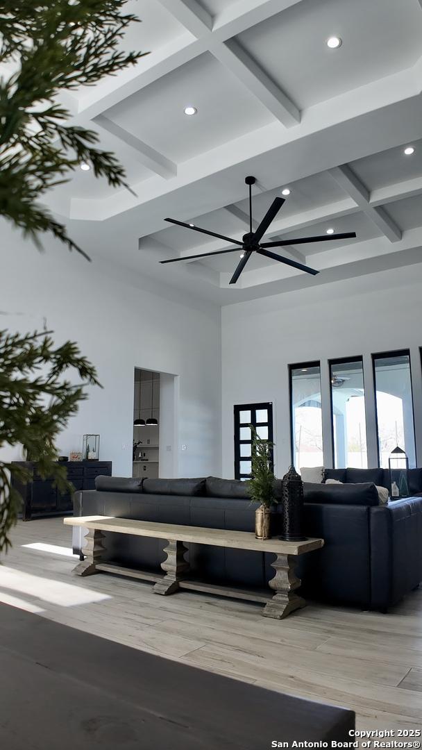 living room featuring coffered ceiling, beam ceiling, ceiling fan, and a towering ceiling