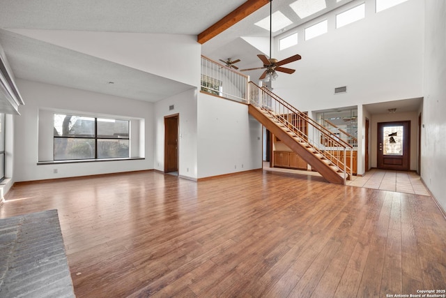 unfurnished living room with beam ceiling, ceiling fan, light wood-type flooring, and high vaulted ceiling