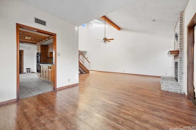 unfurnished living room with lofted ceiling with beams, a brick fireplace, light hardwood / wood-style flooring, a textured ceiling, and ceiling fan