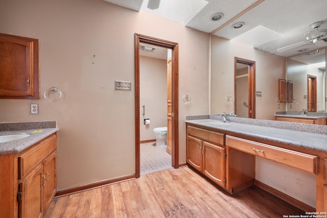 bathroom featuring toilet, wood-type flooring, a textured ceiling, vanity, and ceiling fan