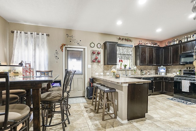 kitchen with tasteful backsplash, light tile patterned floors, black appliances, and a kitchen bar