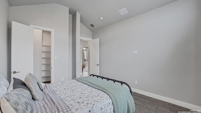 carpeted bedroom featuring a walk in closet, vaulted ceiling, and a closet