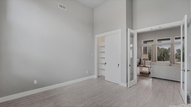 unfurnished bedroom with light hardwood / wood-style flooring, french doors, and a high ceiling