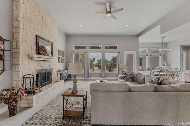 living room with a stone fireplace, ceiling fan, and light wood-type flooring