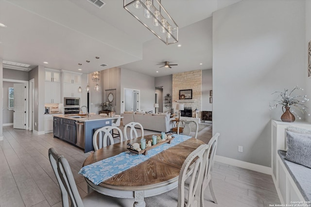 dining room with ceiling fan, a fireplace, light hardwood / wood-style floors, and sink