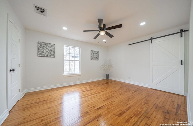 empty room featuring ceiling fan, a barn door, and light hardwood / wood-style flooring