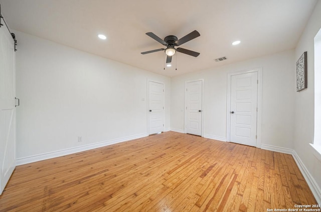 unfurnished bedroom with multiple closets, ceiling fan, a barn door, and light hardwood / wood-style flooring