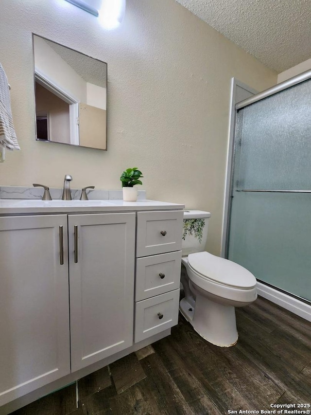 bathroom featuring a shower with shower door, hardwood / wood-style flooring, vanity, toilet, and a textured ceiling