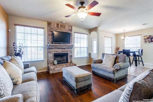 living room with dark hardwood / wood-style flooring, a brick fireplace, and ceiling fan with notable chandelier