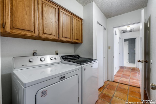 clothes washing area with independent washer and dryer, light tile patterned floors, cabinets, and a textured ceiling