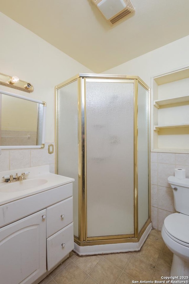 bathroom with tile patterned floors, toilet, a shower with shower door, and tile walls