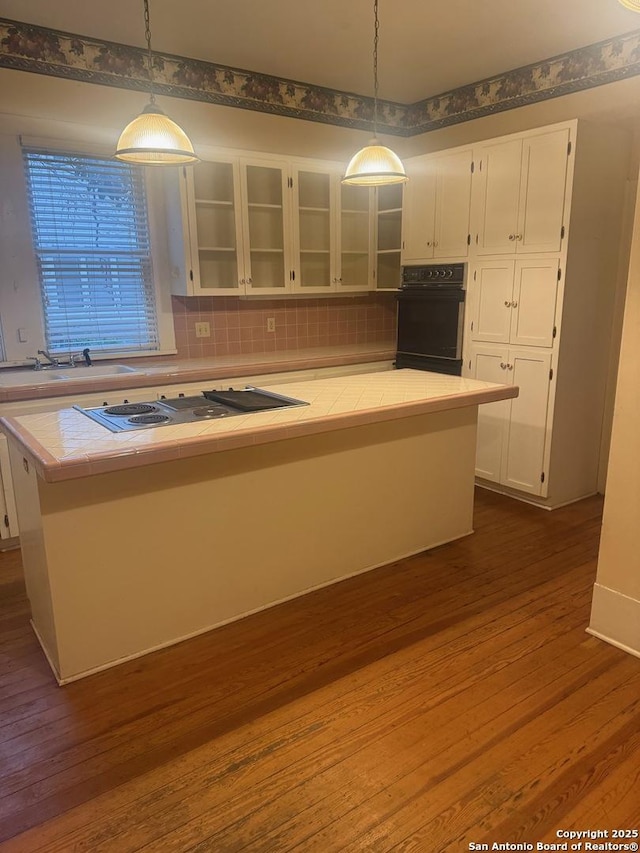 kitchen featuring white cabinetry, tile countertops, black oven, pendant lighting, and decorative backsplash