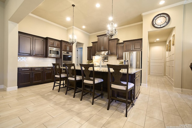 kitchen featuring light stone counters, tasteful backsplash, dark brown cabinets, appliances with stainless steel finishes, and a kitchen island with sink