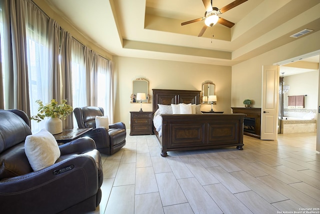 bedroom with a tray ceiling, ceiling fan, and ensuite bathroom