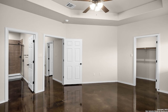 unfurnished bedroom featuring ensuite bath, a raised ceiling, ceiling fan, and a spacious closet