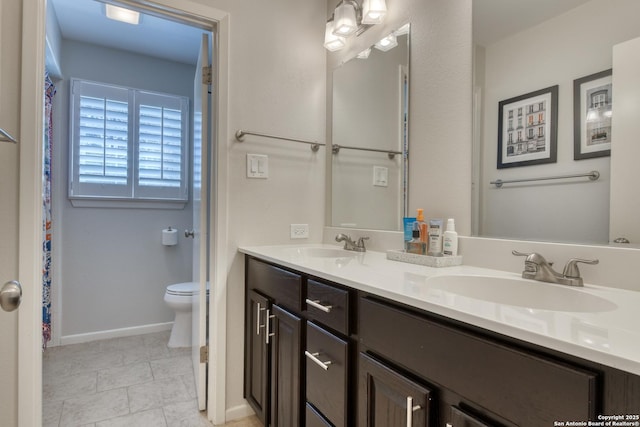 bathroom featuring baseboards, a sink, toilet, and double vanity