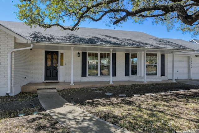 view of exterior entry featuring covered porch, brick siding, roof with shingles, and a garage