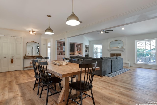 dining space with a ceiling fan, light wood-type flooring, a brick fireplace, and ornamental molding