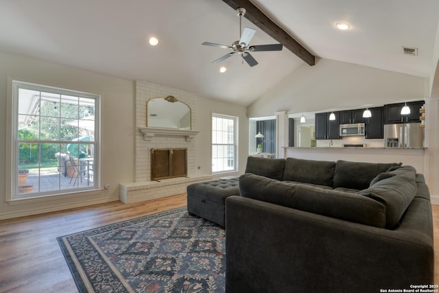 living room with a brick fireplace, visible vents, light wood-style floors, and beam ceiling