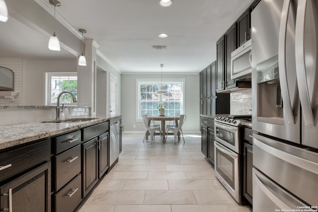 kitchen with light stone counters, crown molding, tasteful backsplash, appliances with stainless steel finishes, and a sink