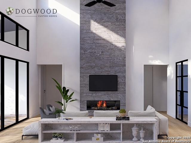 living room featuring ceiling fan, a large fireplace, light hardwood / wood-style flooring, and a high ceiling